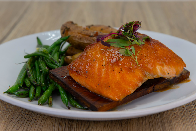 Cedar Plank Grilling showing a serving of salmon on a plate, complete with small charred plank below.