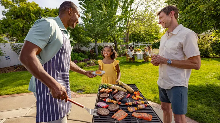 Young girl watching two older men grill outside.