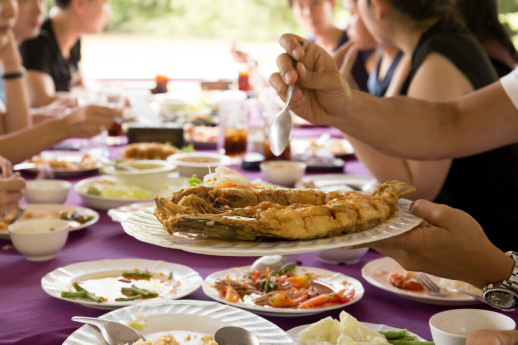 Group of friend enjoying lunch with hand holding deep fried fish in thai style