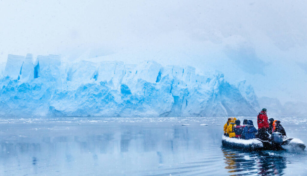 Snowfall over the boat with frozen tourists driving towards the huge blue glacier wall in the background, near Almirante Brown, Antarctic peninsula