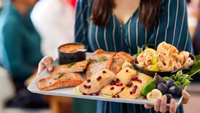 Reasons to love fish with a woman holding a platter of different cooked fish and sauce.