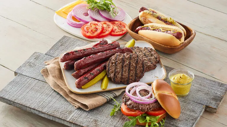 Cooked bison hot dogs and burger patties surrounded by condiments.